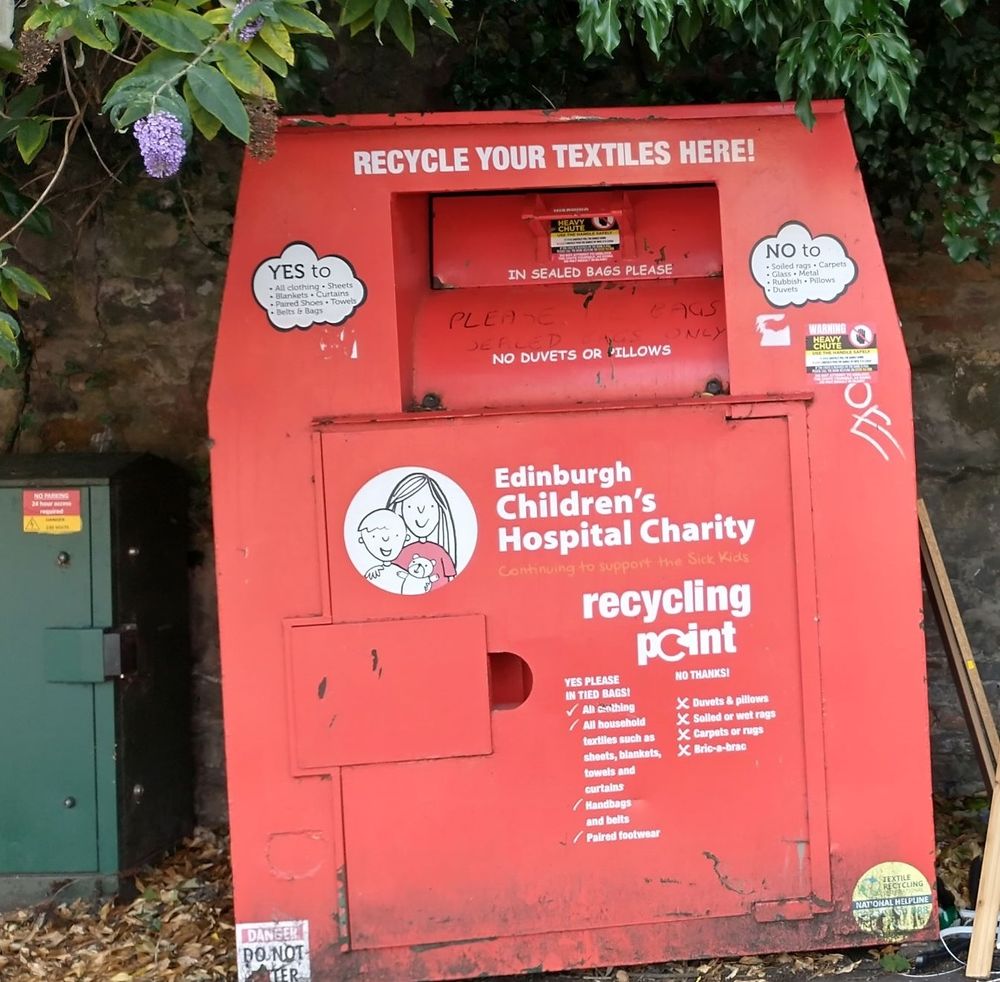 Large red metal container with hatch at the front. White lettering gives instructions and information that it's 'Edinburgh Children's Hospital Charity Recycling Point' for textiles.