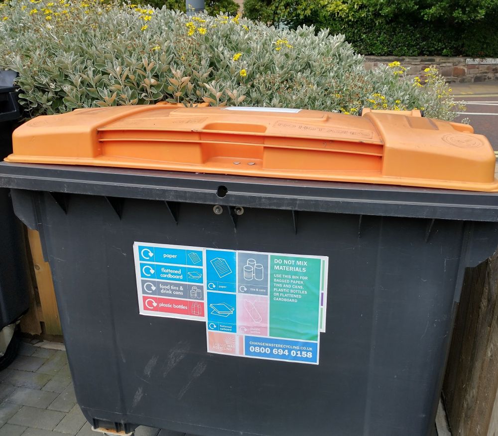 Large dark grey bin with orange lid. Notices on the side give instructions for use.