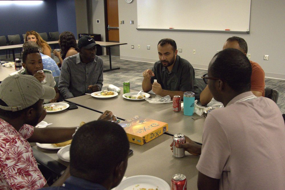 Group of scholars gathered together socializing at tables eating food.