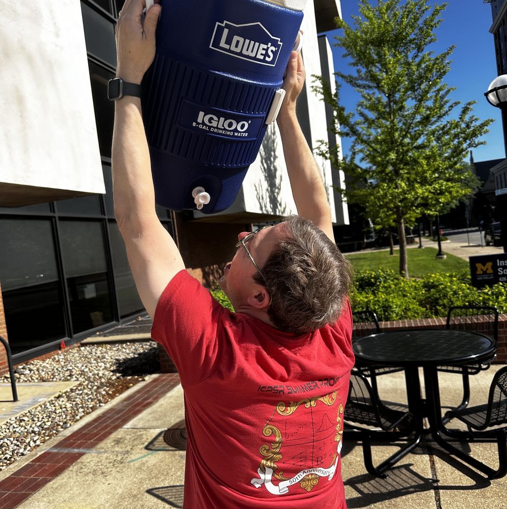 A man holding up a cooler, acting as though he's drinking straight from the spout