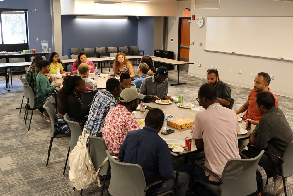 Group of scholars gathered together socializing at tables eating food.