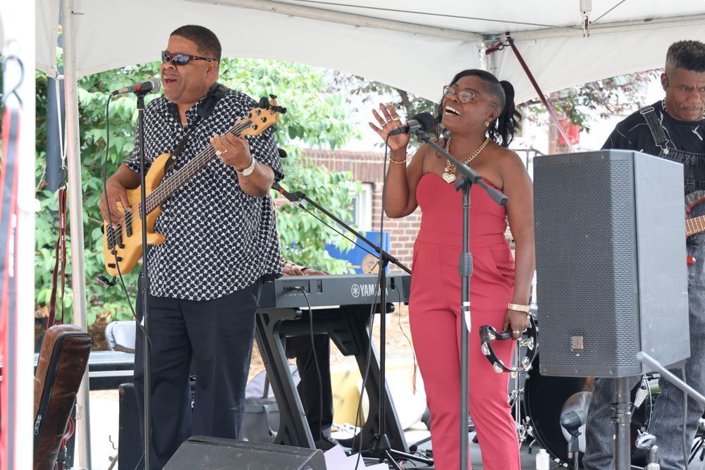 A man playing bass and a woman with a tambourine, both singing. 