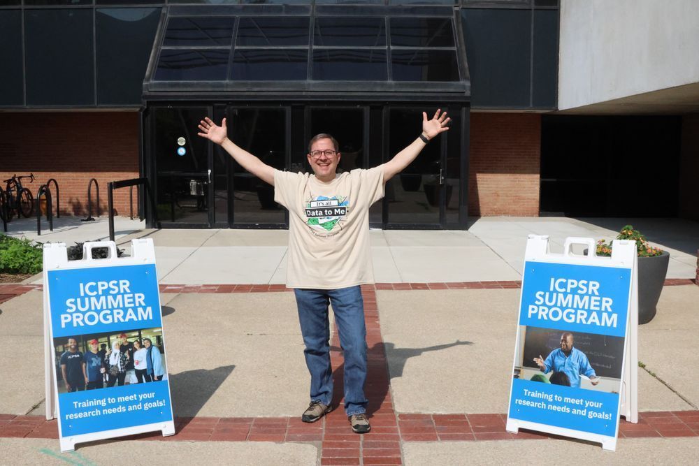 A man stands proudly in front of two ICPSR signs, stretching his arms out in celebration