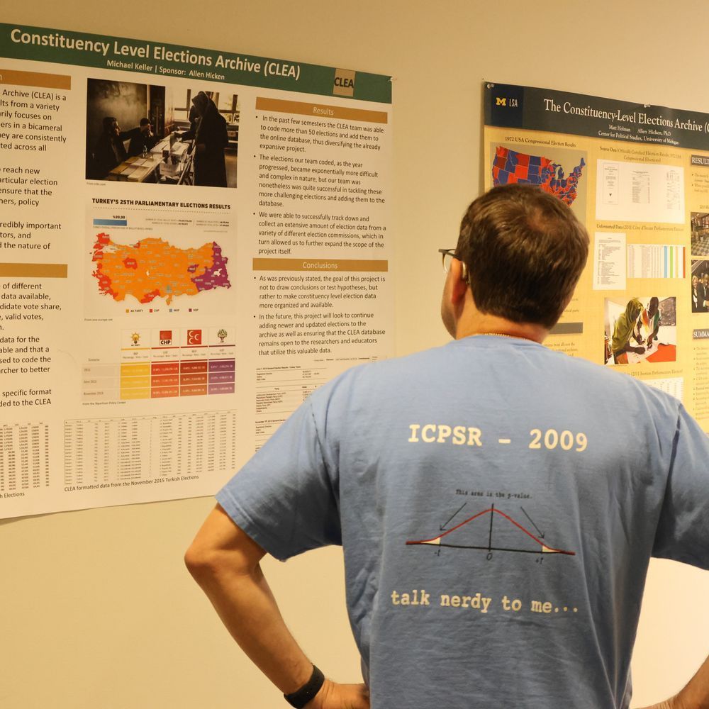A man examines a poster while showing off the back of his shirt