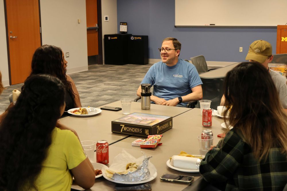 Group of scholars gathered together socializing at tables eating food.