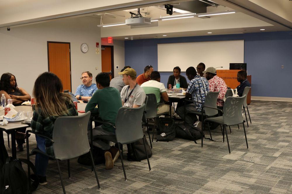 Group of scholars gathered together socializing at tables eating food.