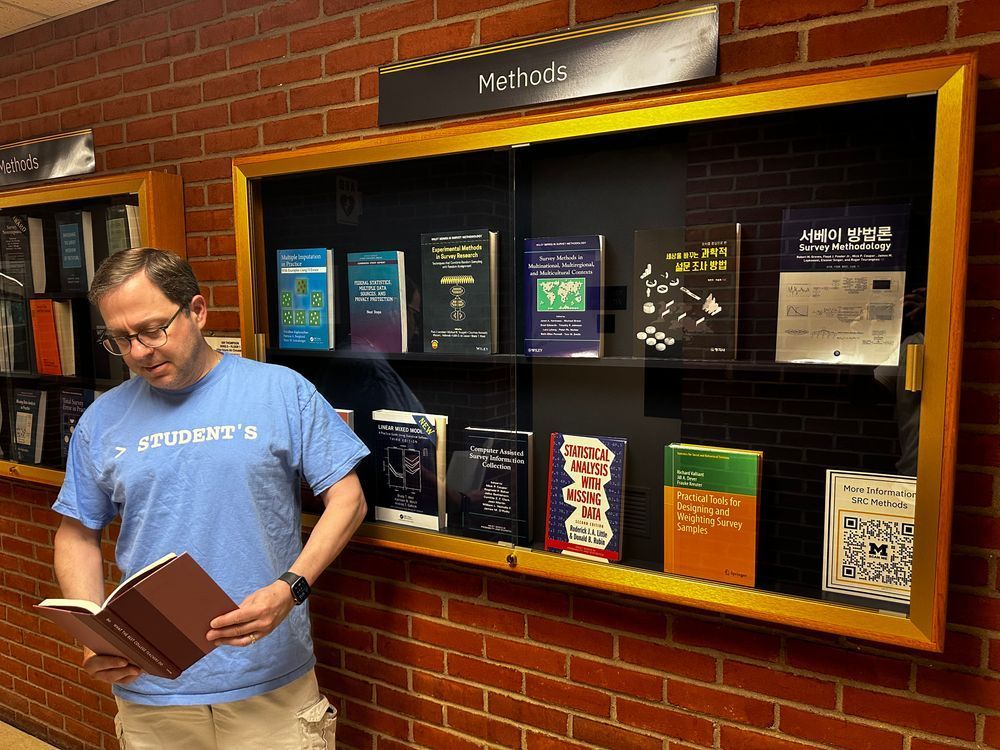 A man in front of a methods bookcase, reading a book on being a great professor