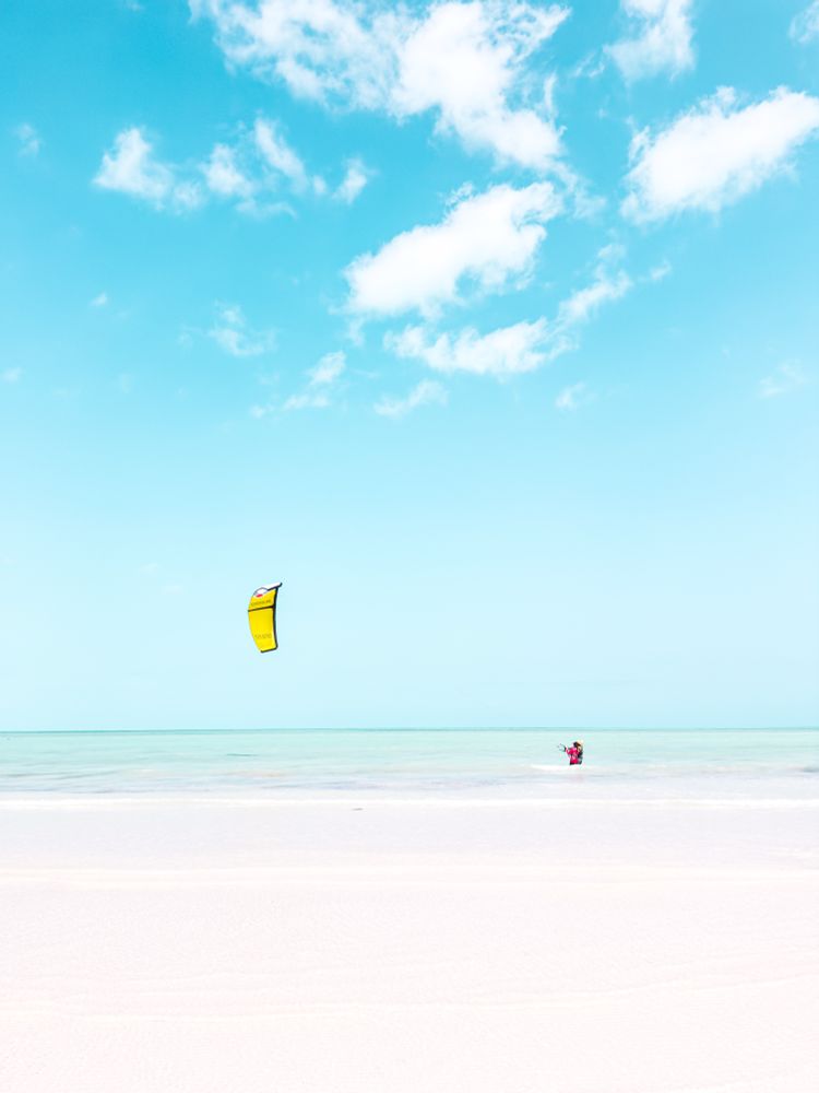 A low contrast white sandy beach and a blue sky with a kite surfer
