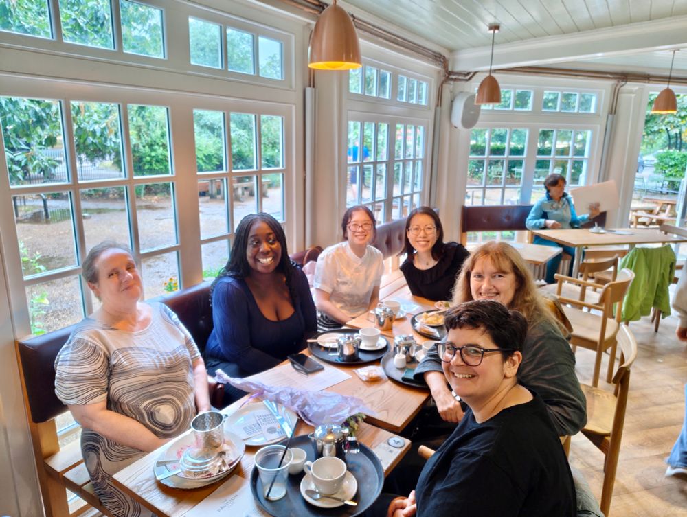 A picture of 6 people all sat round a table in a cafe, smiling at the camera

