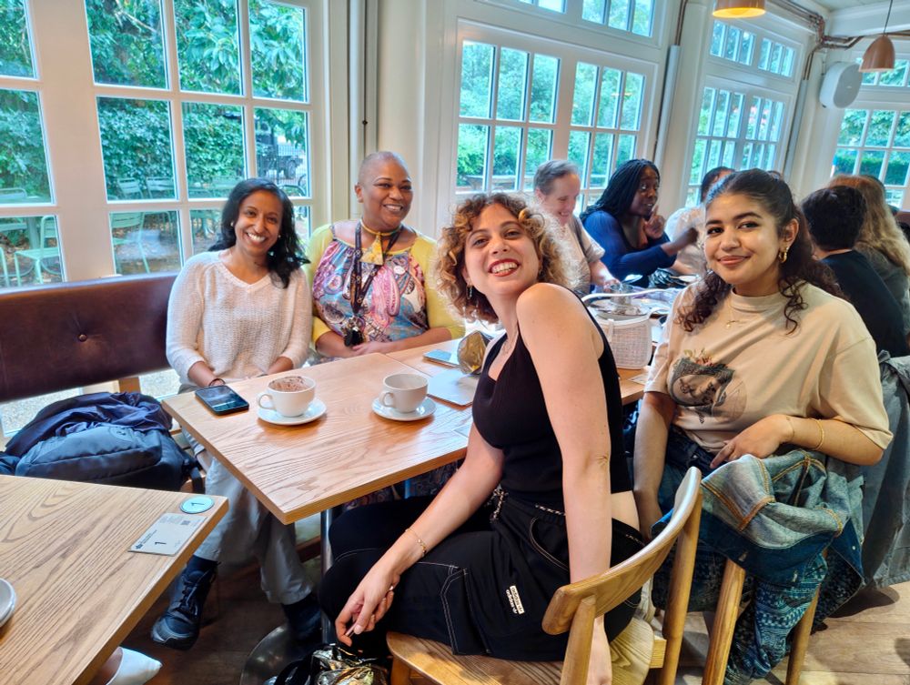 A picture of 3 people sat at a cafe table, smiling to camera
