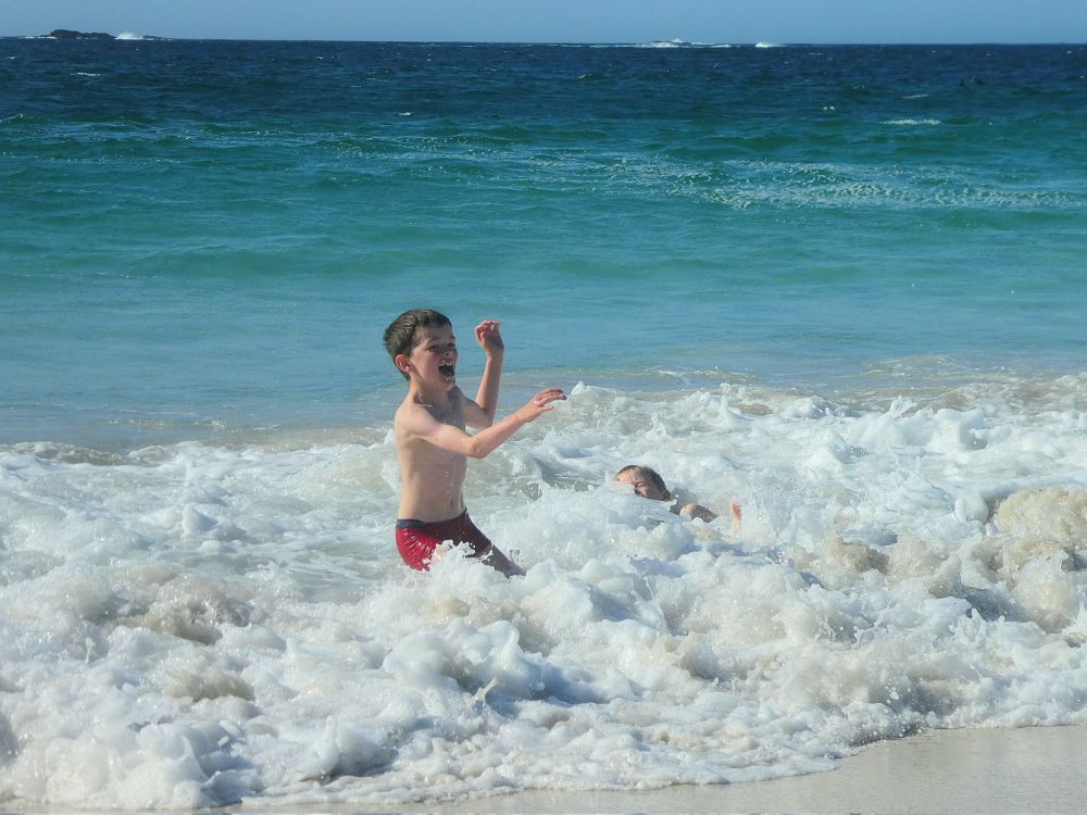 Young boy running from waves on right his brother has fallen into the sea foam