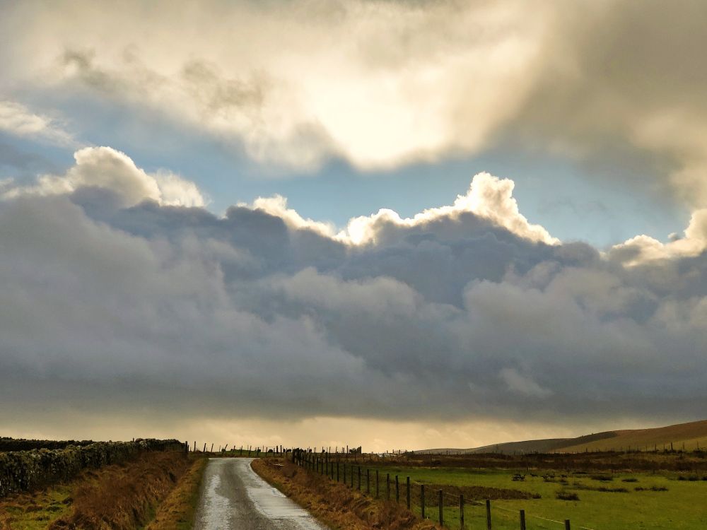 Dark clouds and golden light over a rural road with fields either side