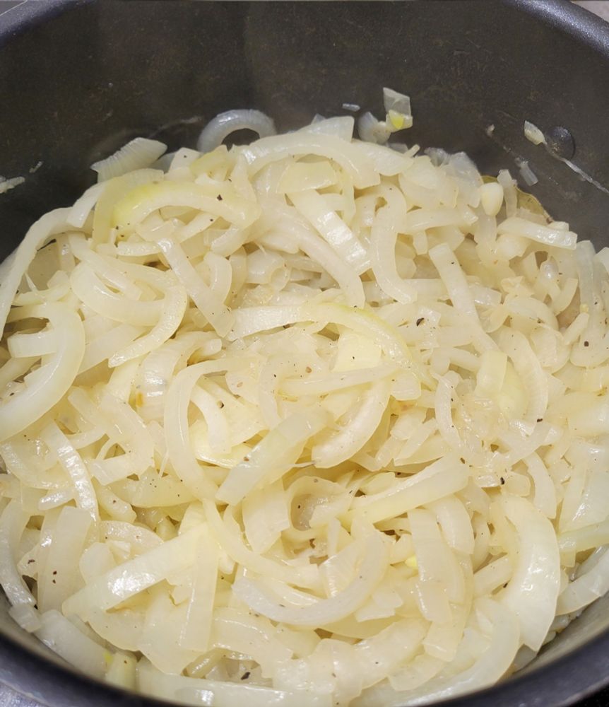 Photograph of a pan filled with sliced onions, slowly cooking down to a soft delicious mass