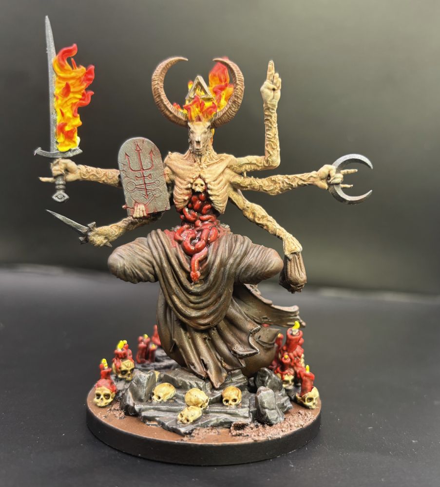 A painted model figure of a grotesque sorcerer with six arms, a goat skull face, and just all sorts of horror stuff going on.