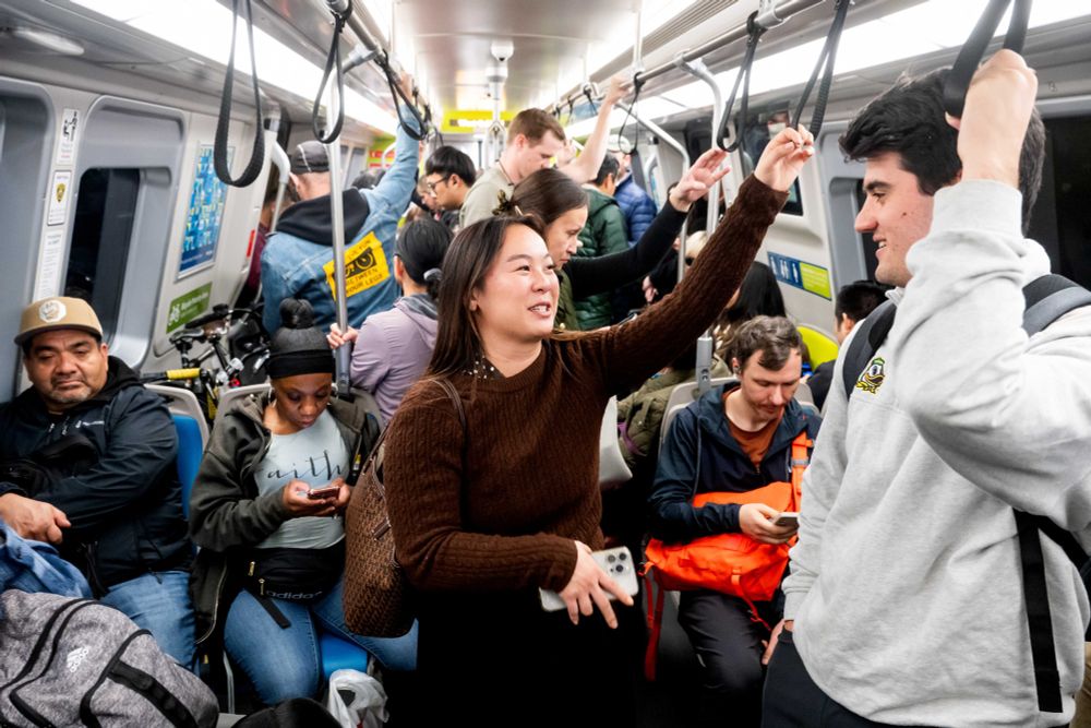 Crowded train with riders chatting and hanging onto straps.