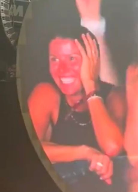 A woman looking more embarrassed than she's ever been in her life, in a black tank top and a hand on the side of her head