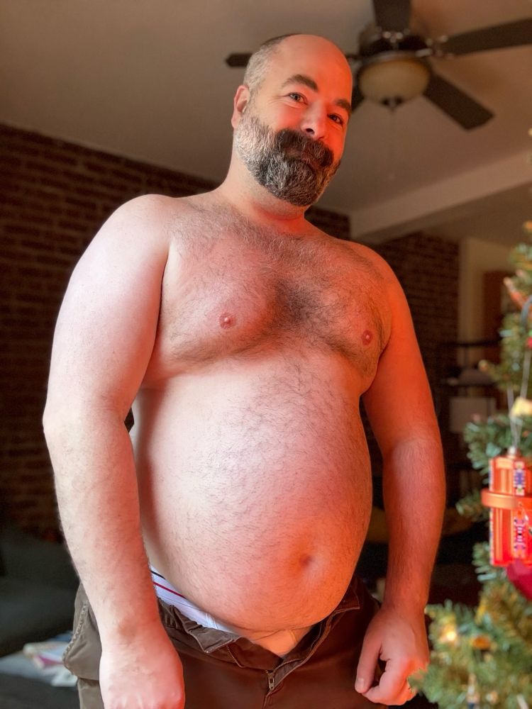 A shirtless selfie of me smiling, my big belly lit by the glow of our Christmas tree. Shorts are unbuttoned and my whitey tighties are just barely visible.