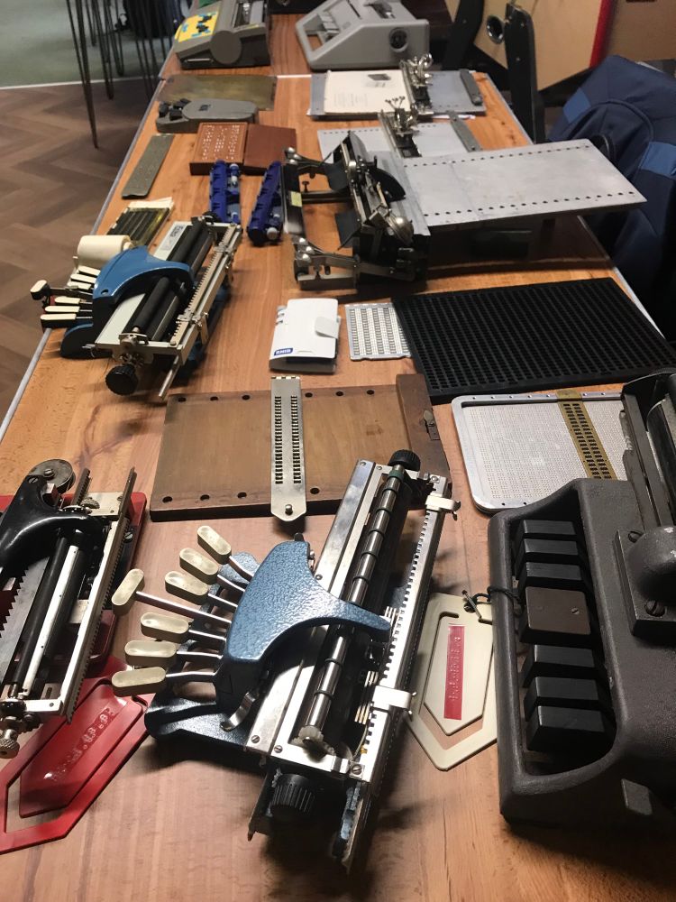 Table displaying heritage braille equipment, including a Hall Braille Writer, Stainsby, and various hand frames