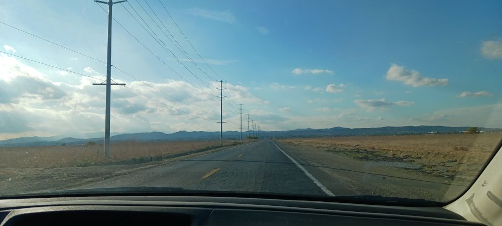 Photo taken out of a car window showing a blue sky and the open road.