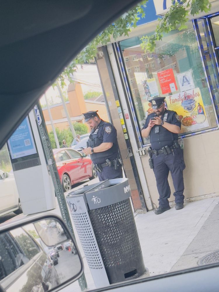 Two NYPD cops on the street, looking at their phones. 