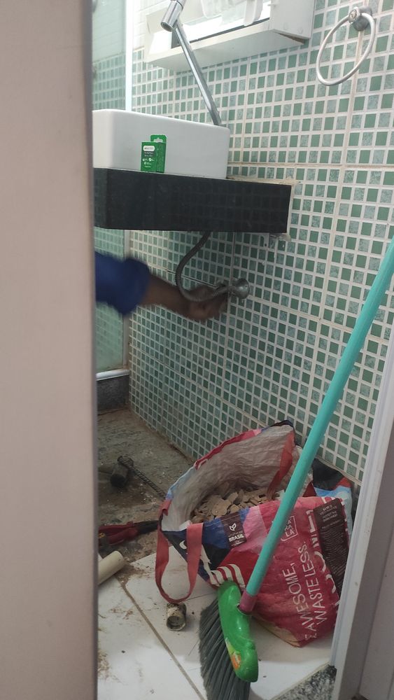 Mãos do pedreiro trabalhando no encanamento debaixo da pia do banheiro