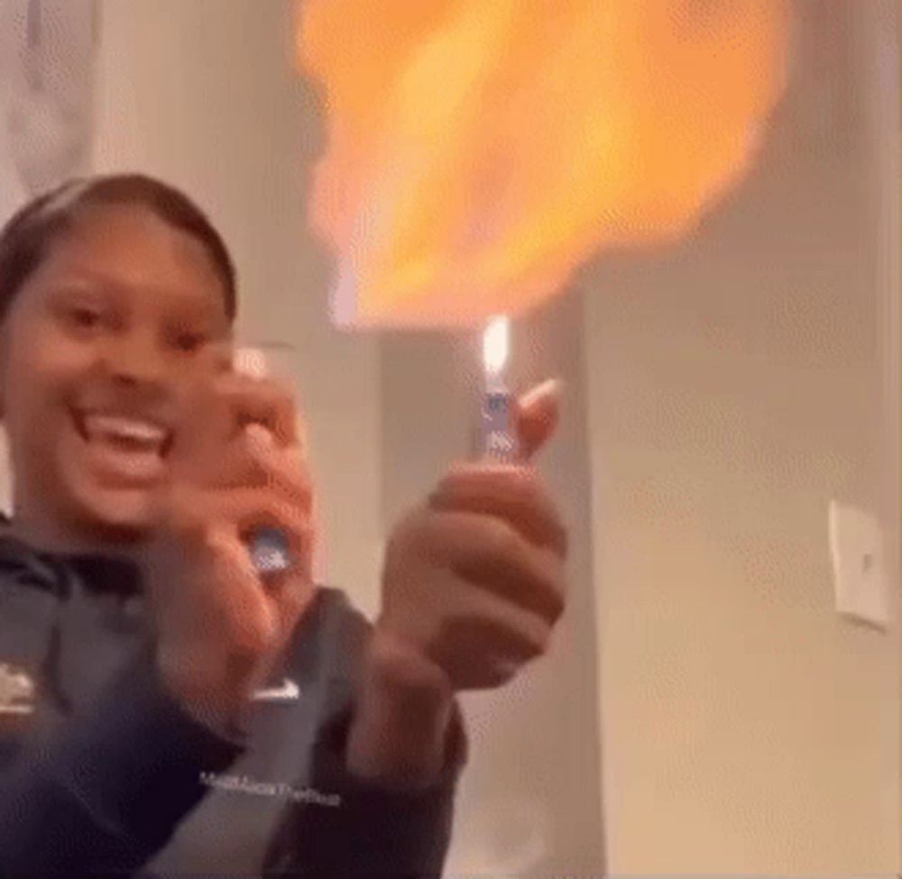 a woman is holding a lighter with flames coming out of it and smiling .