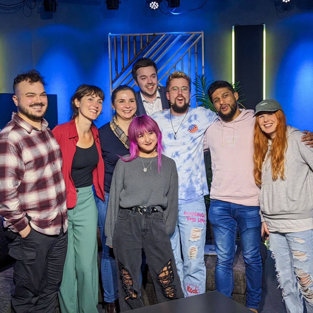 Eine Gruppe von Menschen die in einem Studio steht und in die Kamera lacht.
