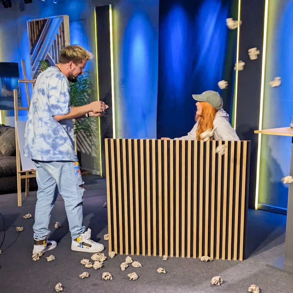 Zwei Menschen in einem Studio die mit Papierbällchen abgeworfen werden.