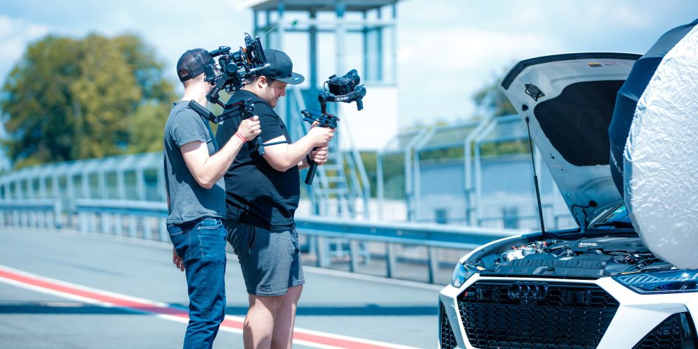 Zwei Kameramänner vor einem Auto mit offener Motorhaube