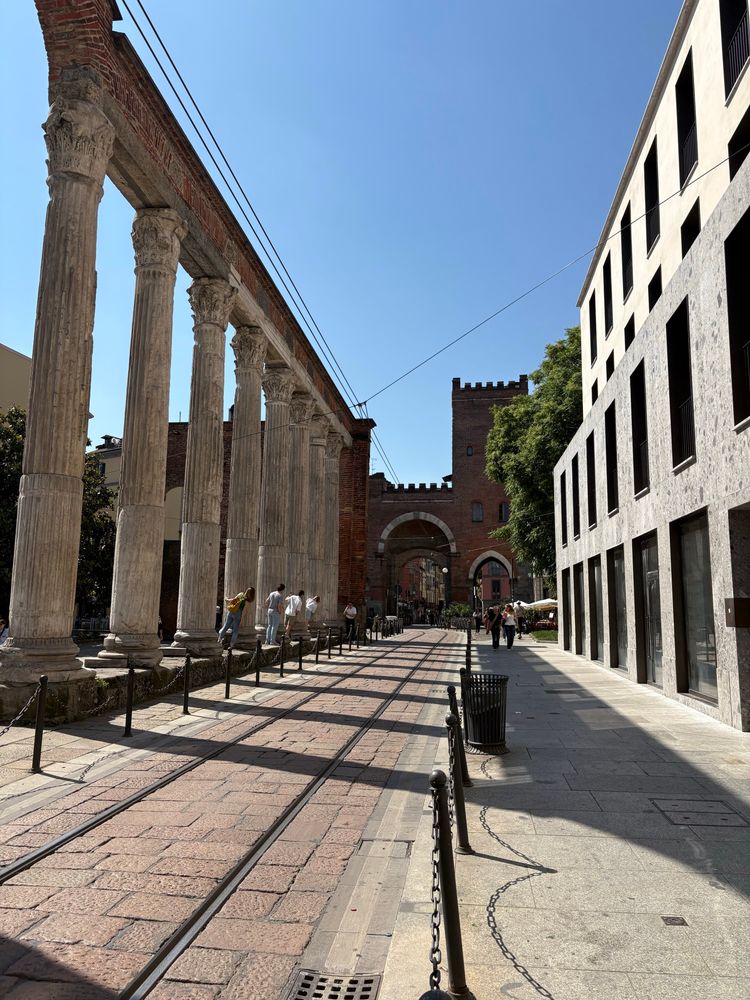 Picture of a touristic place in Milan (Colonne dj San Lorenzo) where someone is taking a photo of 4 people peeking out of the Roman columns