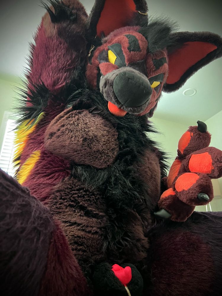A hyena fursuit with a plush sheath raising his arm to the viewer.