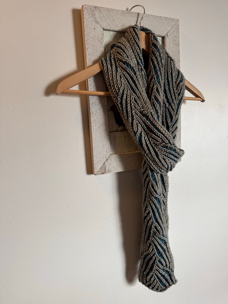 Brioche knit scarf with a faux braid pattern using grey and blue yarn. Scarf is draped over a hanger. 