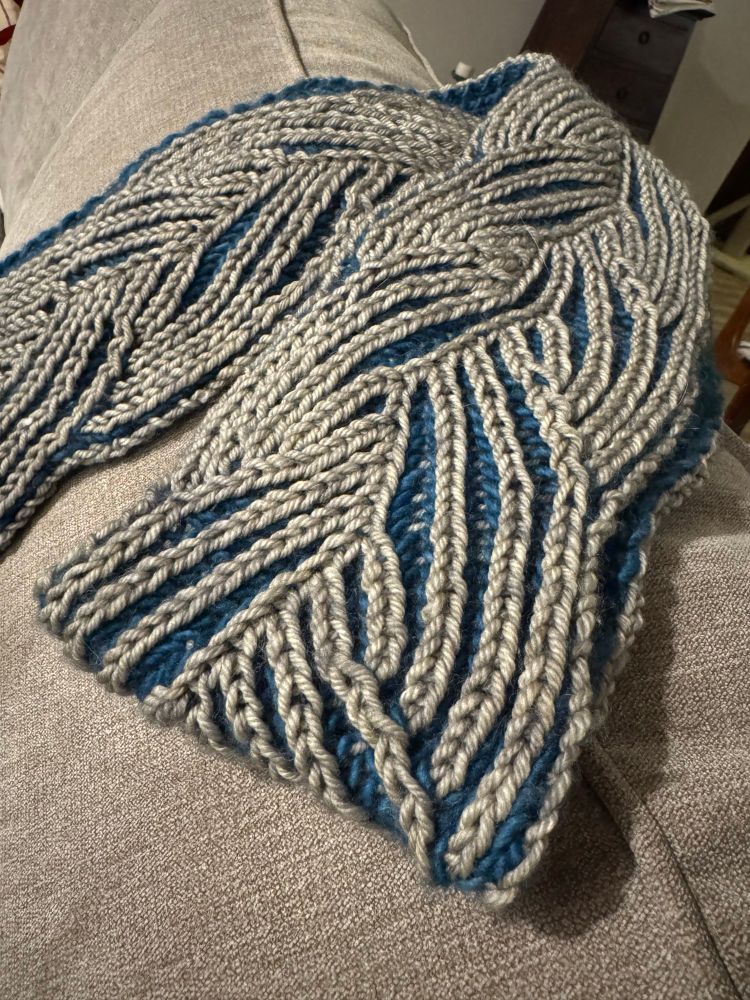 Brioche knit scarf with a faux braid pattern using grey and blue yarn. Close up draped across the back of a couch.  