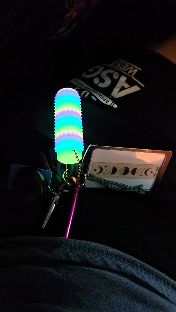 A pink carabiner with a ton of keys, a key card with a textured sticker on it, and a glowing rainbow-striped cylinder with spikes. 