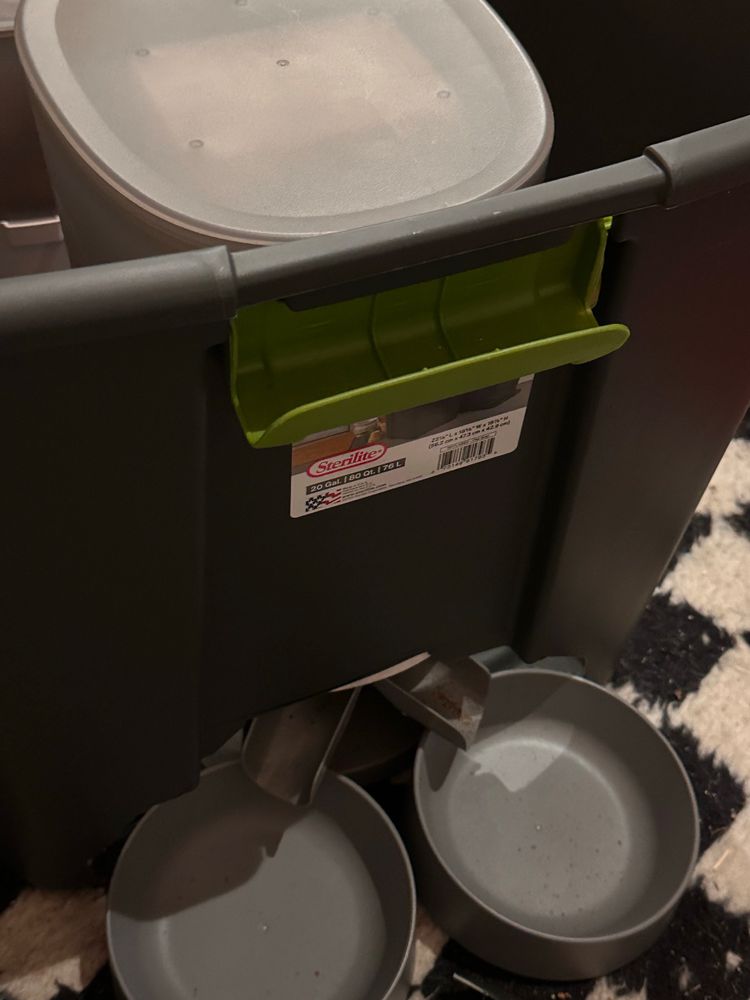 A plastic bin with a hole cut at the bottom for an automatic pet food feeder inside to stick out the bottom.  