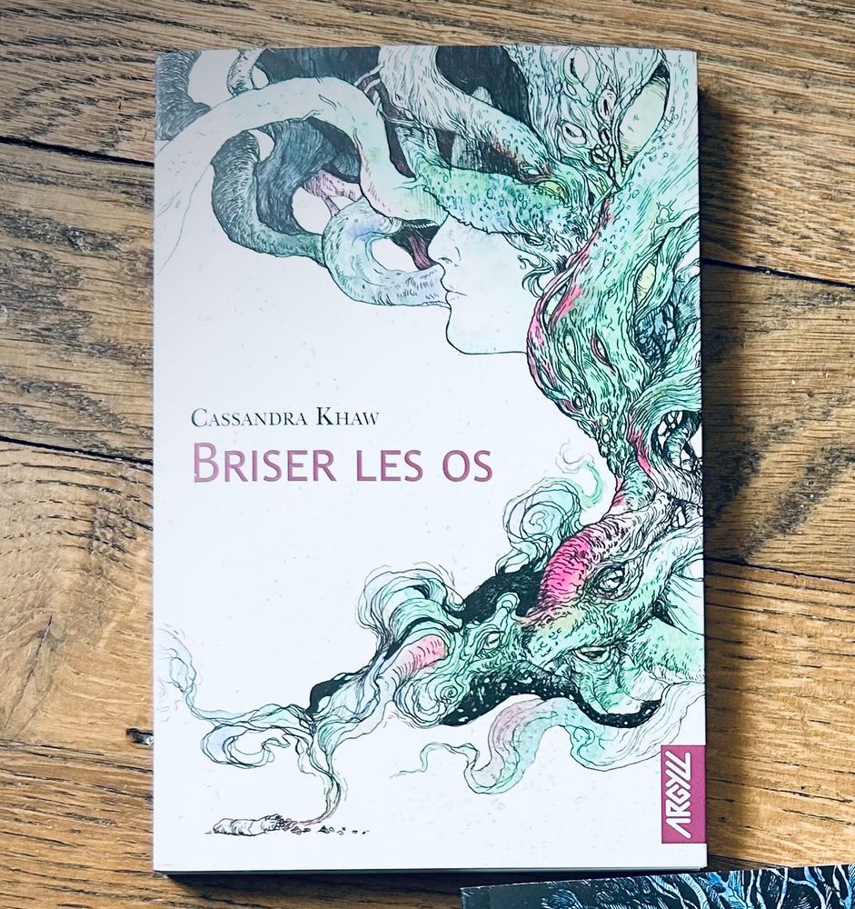 Couverture du livre Briser les os de Cassandra Khaw, avec une illustration représentant un profil humain se fondant dans des tentacules et formes végétales colorées en vert, rose et noir.