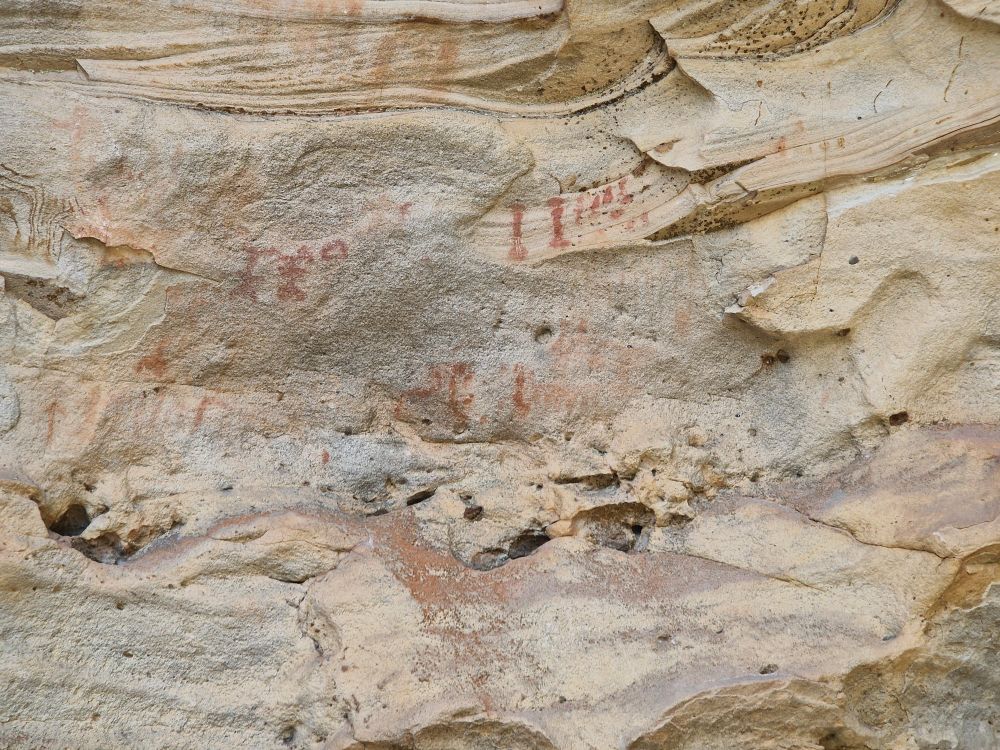 Various cave painting in red on a cave wall.