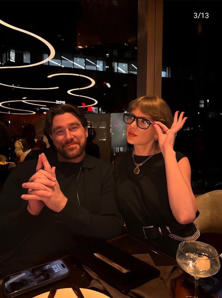 Travis kelce and Taylor swift in a restaurant both wearing full black outfits and Taylor wearing glasses