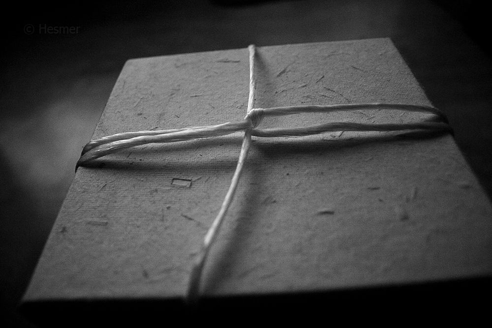 Schwarzweiße Nahaufnahme. Ein Karton aus grobem Papier, um aus weißes Paketband geschnürt ist, um den Deckel zu sichern.