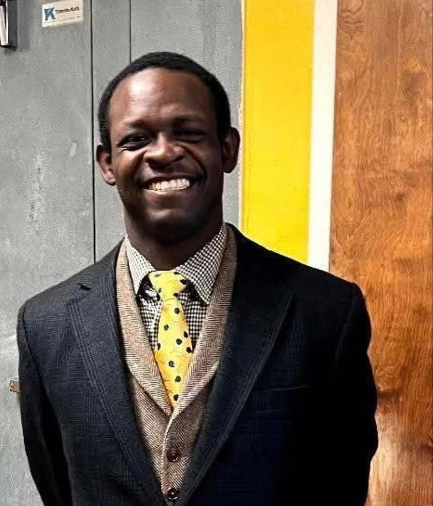Photo of a young Black man Jayvon Givan. He is smiling happily. He is wearing a suit and blazer with a yellow tie.