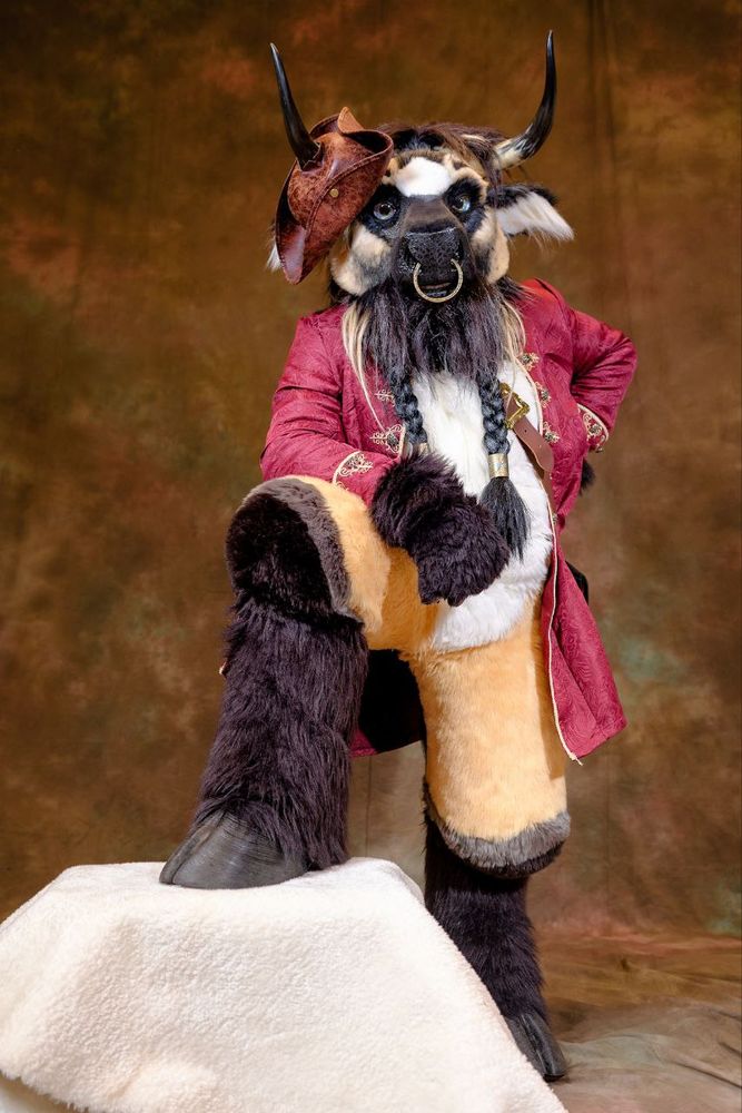 Photo of a bull fursuit with propped up leg, wearing a pirate jacket and hat.