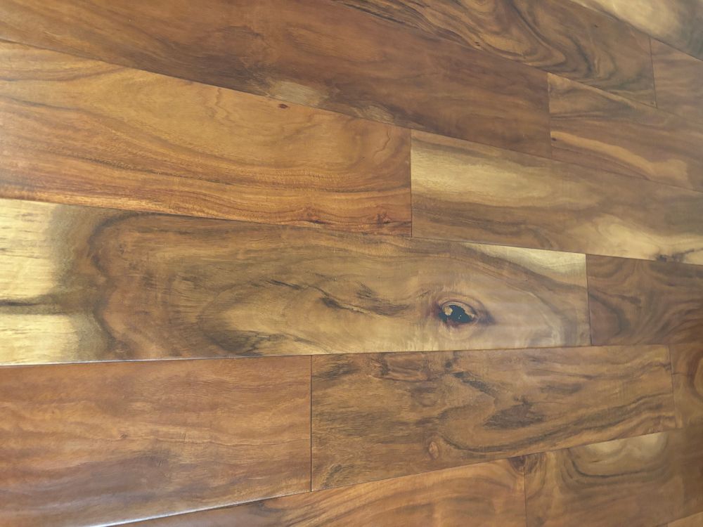 Slats of patterned acacia wood flooring with swirls of light to dark espresso colors. Center is a knot that looks like an eye and light space that looks like the long face of Falkor from Neverending Story. 