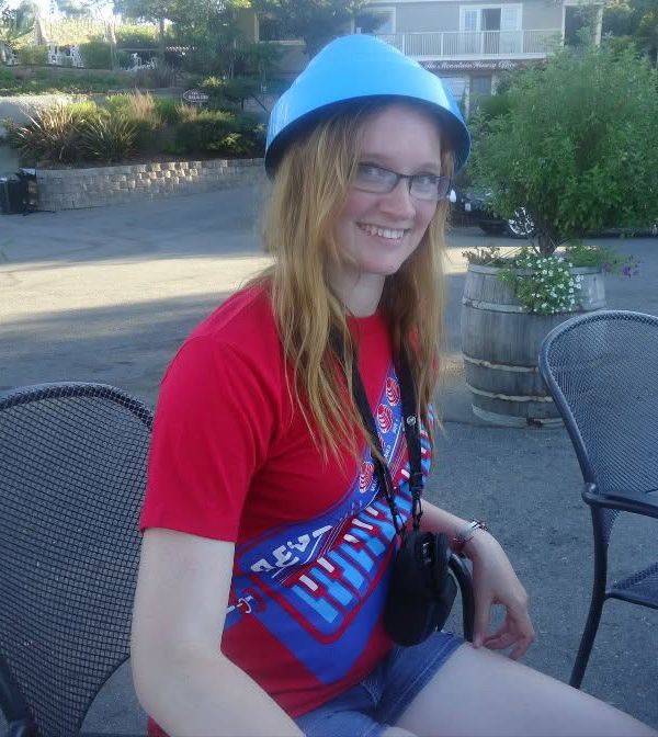 A young Allison is wearing a red Devo shirt, with an old digital camera case hanging from her neck. She is wearing a blue Devo Energy Dome. 