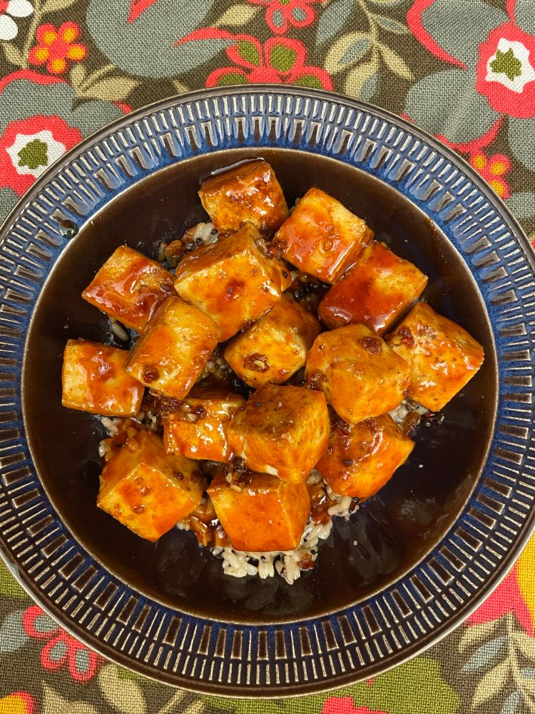 Tofu over brown rice with chili/soy/lime oil and maple Gochujang sauce in a Blue and brown bowl with ridge pattern in edges.