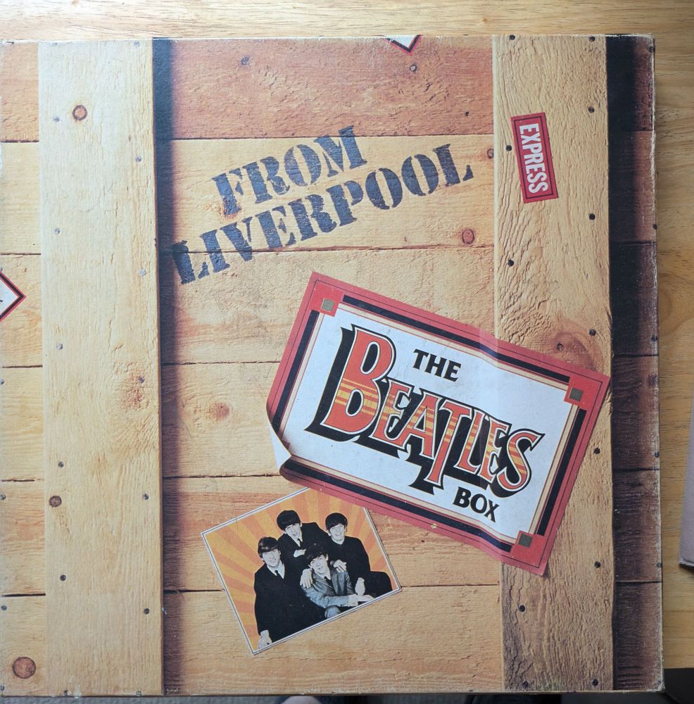 A cardboard box containing vinyl records that looks like a crate with a picture of the band the Beatles on the cover