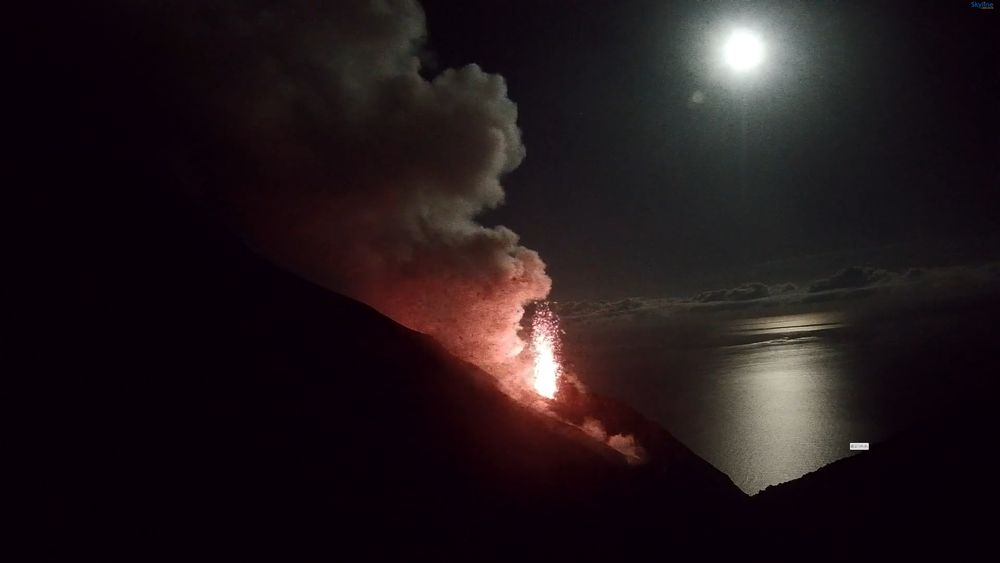 Stromboli erupting as the moon drops toward the sea horizon. 