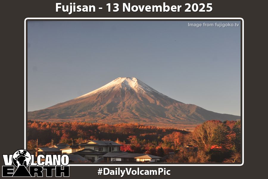 Webcam image of Fujisan - The volcano with its summit covered in snow is seen from the north with the rooftops and treetops of Oshino in the foreground. In the morning light, the red and gold leaves of autumn seem more vivid. 