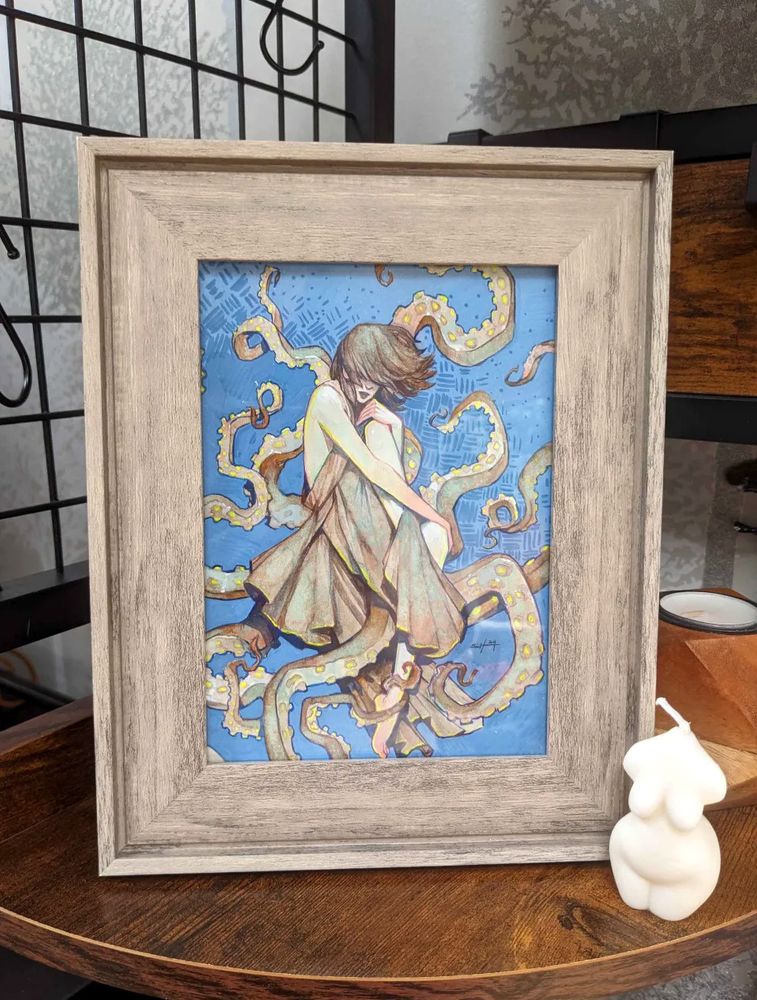 Original painting in a wood frame in situ on a shelf with a curvy figurative candle next to it. The painting in the frame shows a woman with shaggy shoulder-length hair, her face hidden by it, huggin her legs, with cloth wrapped around her, tentacles emerging from behind her and going in all sorts of directions.