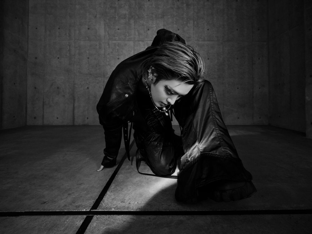 Black and white picture of NCTs Yuta kneeling on one knee, one hand on the ground in an artistic shot for his teaser for the single Twisted Paradise.