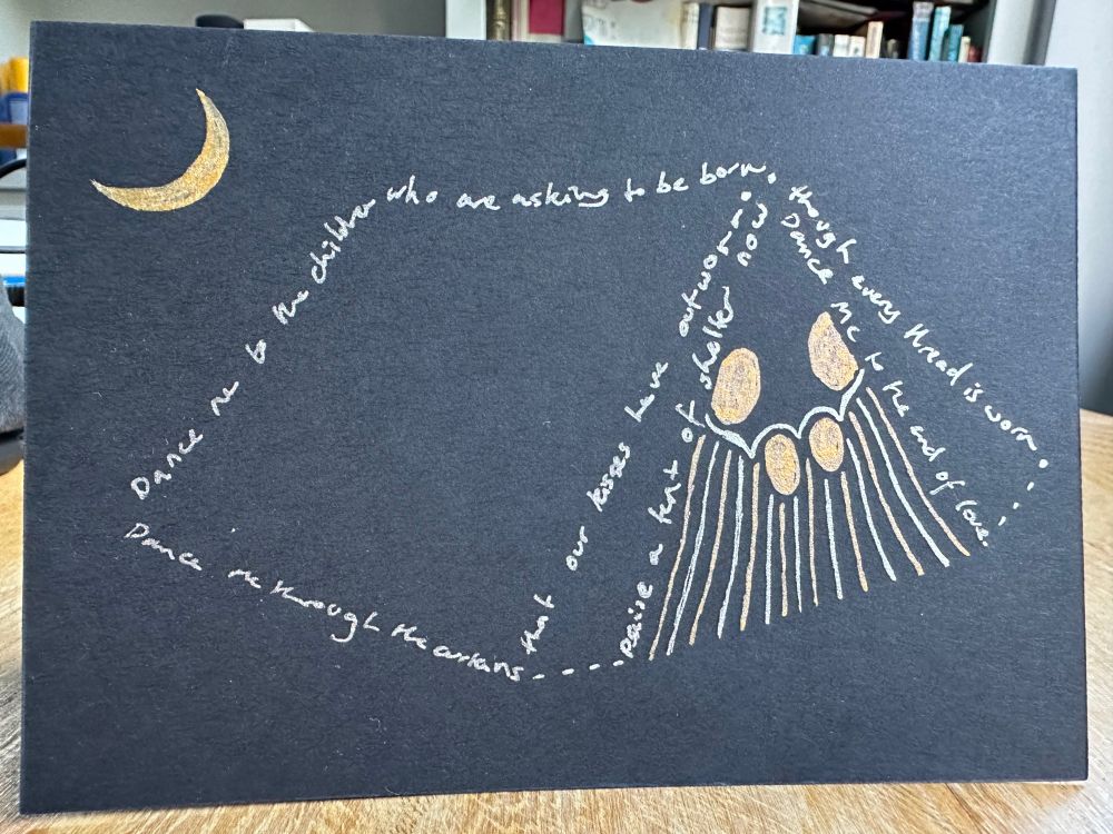 A drawing on black card of a tent with four figures (two big, two small) inside it. The people, and the moon above them, are in gold. The tent outlines are in silver and are a Leonard Cohen verse:
Dance me to the children 
who are asking to be born
Dance me through the curtains 
that our kisses have outworn
Raise a tent of shelter now, 
though every thread is torn
Dance me to the end of love